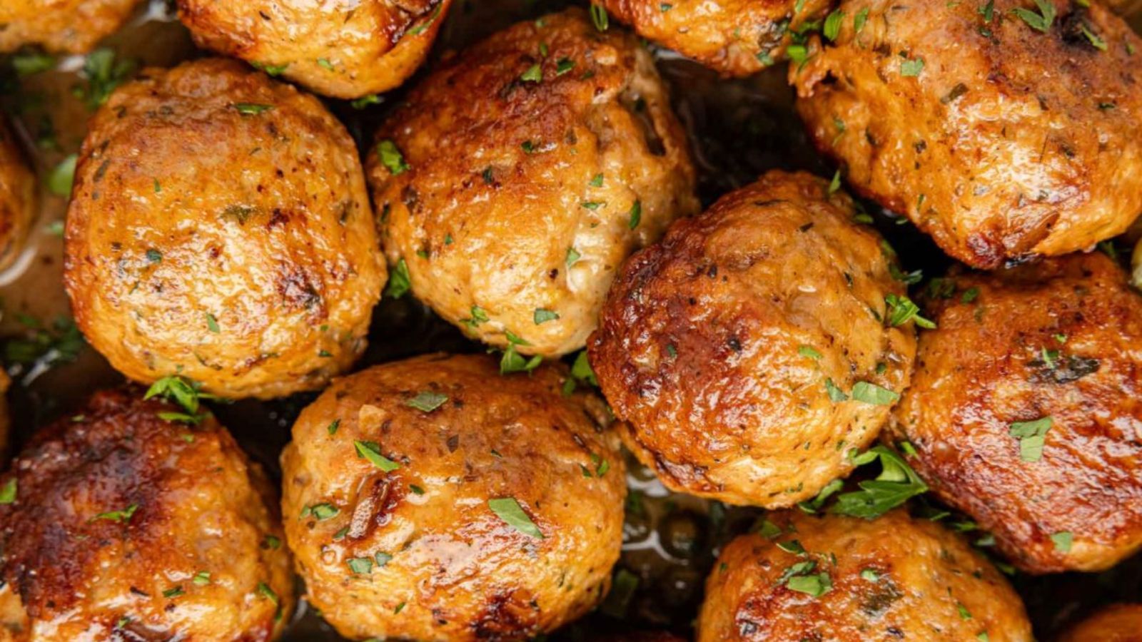 Close-up of cooked meatballs garnished with chopped herbs, showing a browned, crispy exterior.