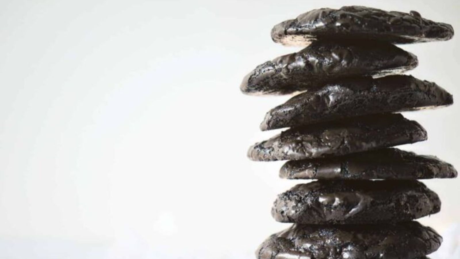 A stack of six dark chocolate cookies is arranged vertically on a light, plain background.
