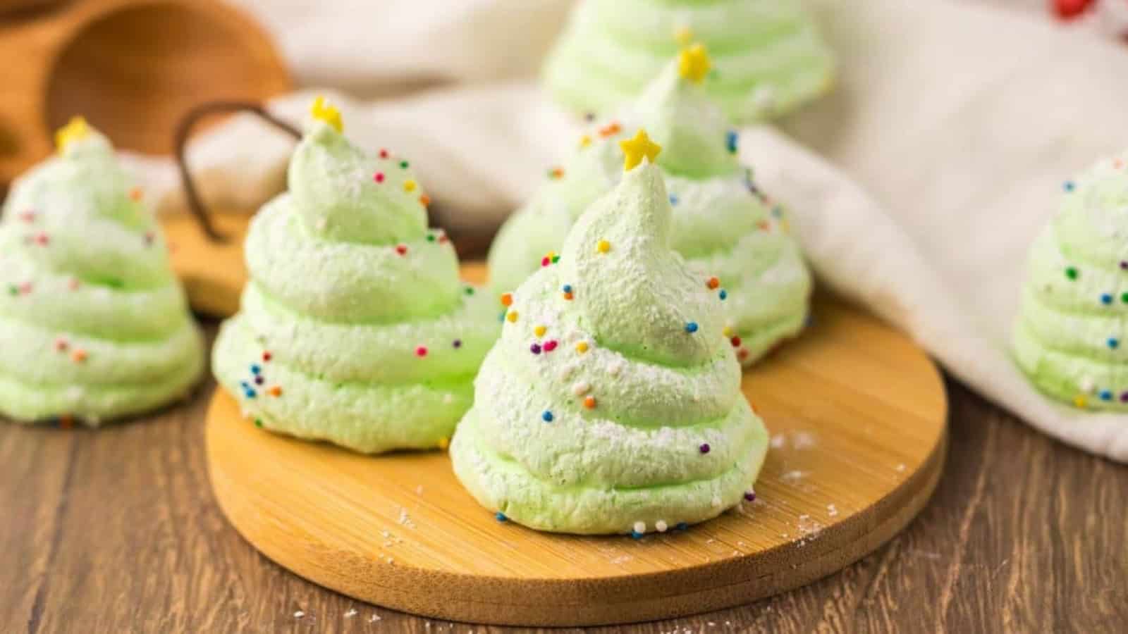 Green Christmas tree-shaped meringues with sprinkles and star toppers on a wooden board.