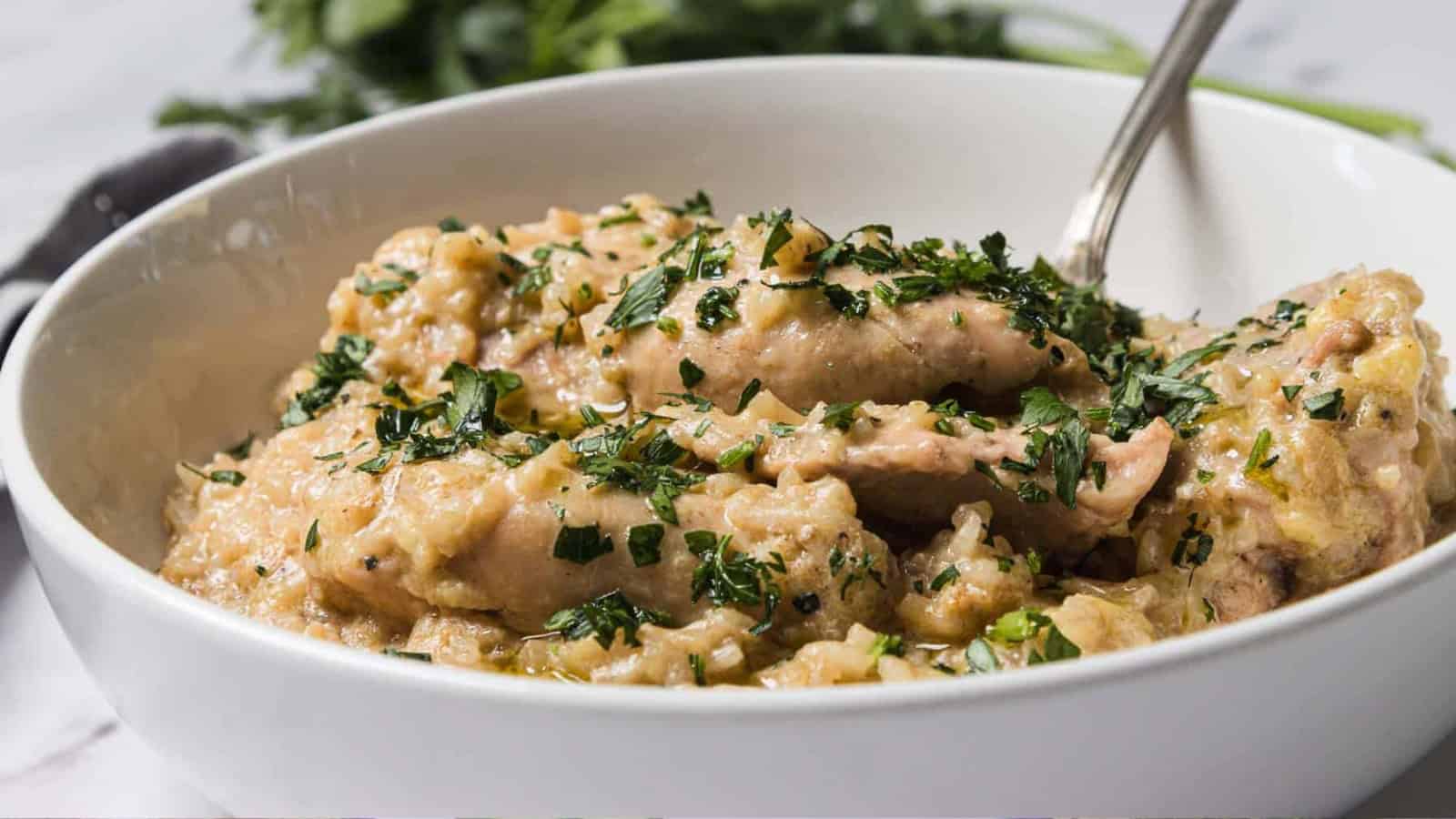 A bowl of creamy chicken stew garnished with chopped herbs and served with a spoon.