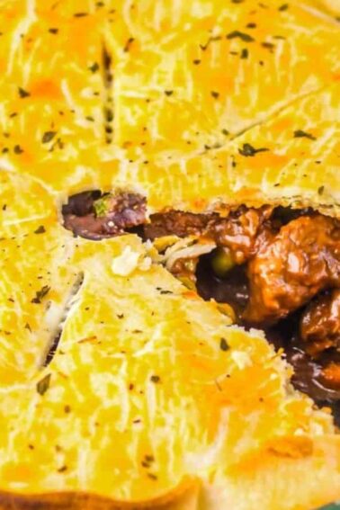 A baked meat pie in a glass dish with a slice removed, revealing chunks of meat, peas, and a rich brown filling inside a golden crust.