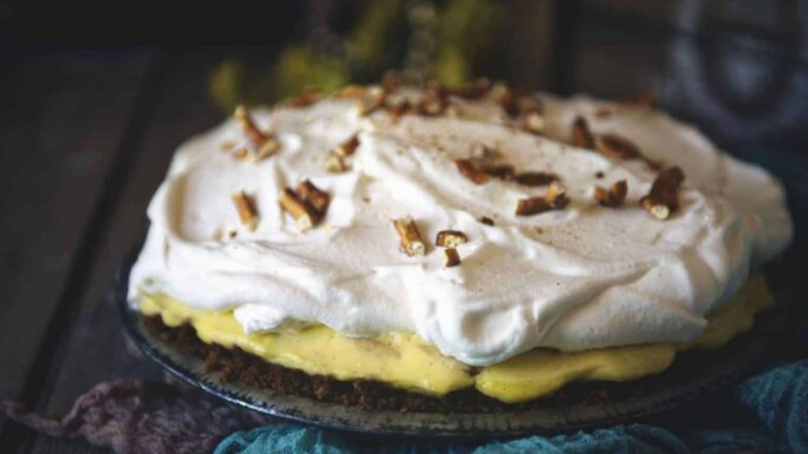 A cream pie topped with whipped cream and chopped nuts sits on a glass plate.