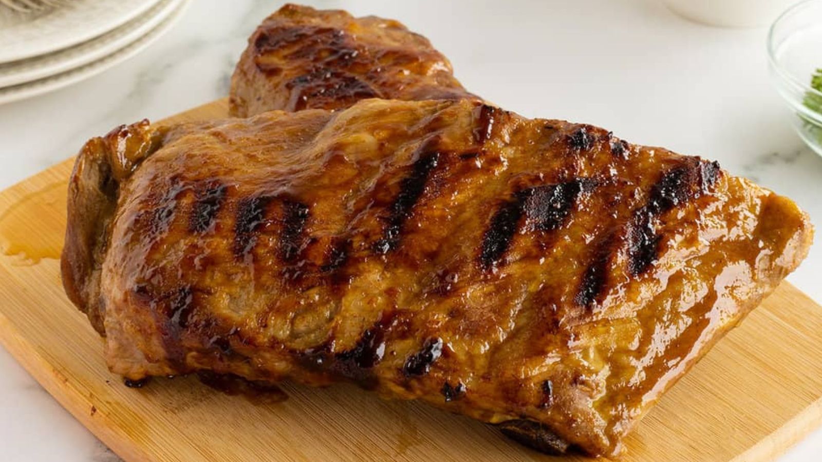 Two pieces of grilled, glazed meat with visible char marks are placed on a wooden cutting board.