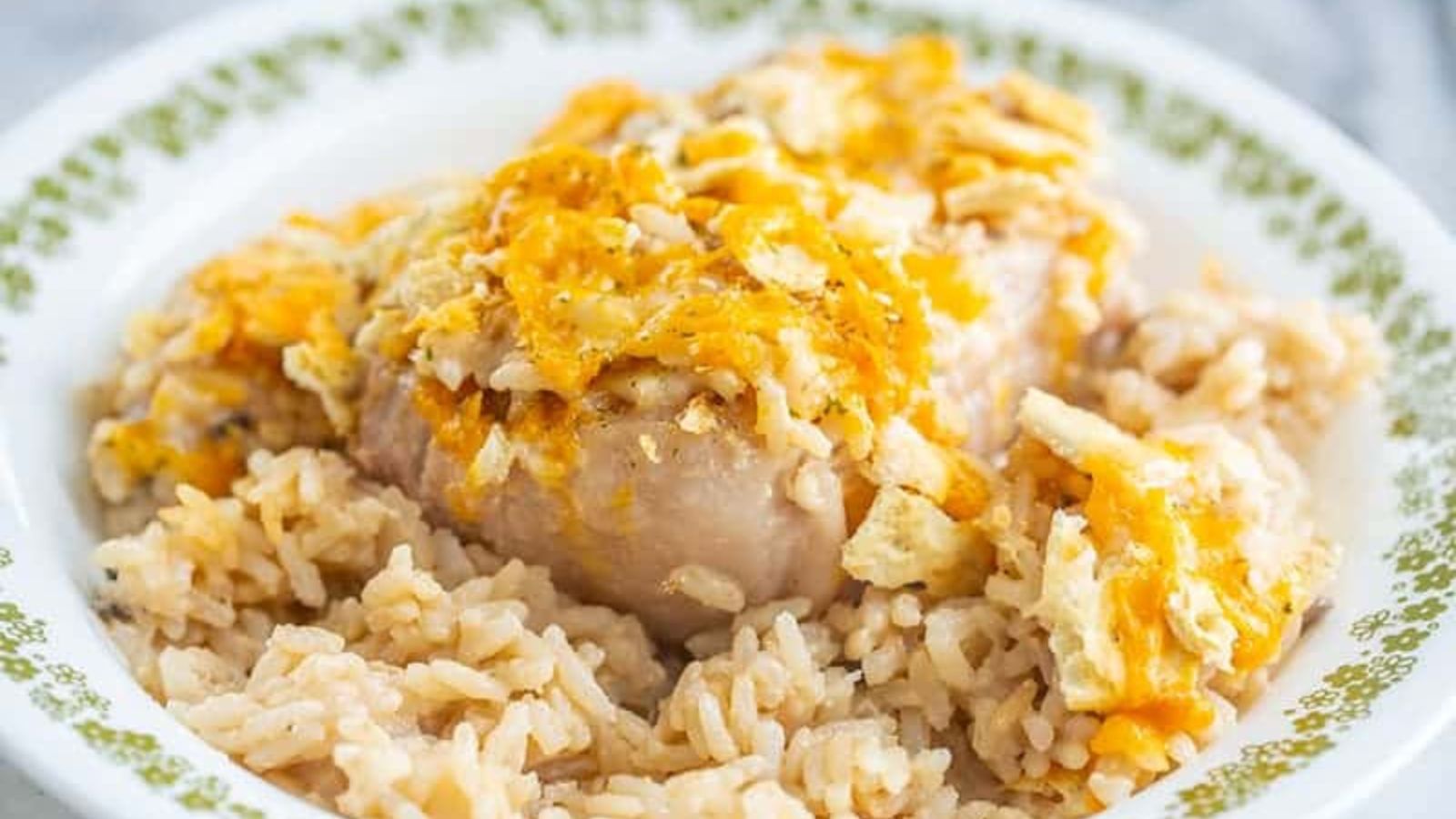 A plate of baked chicken topped with melted cheese and crushed chips, served over a bed of seasoned rice.