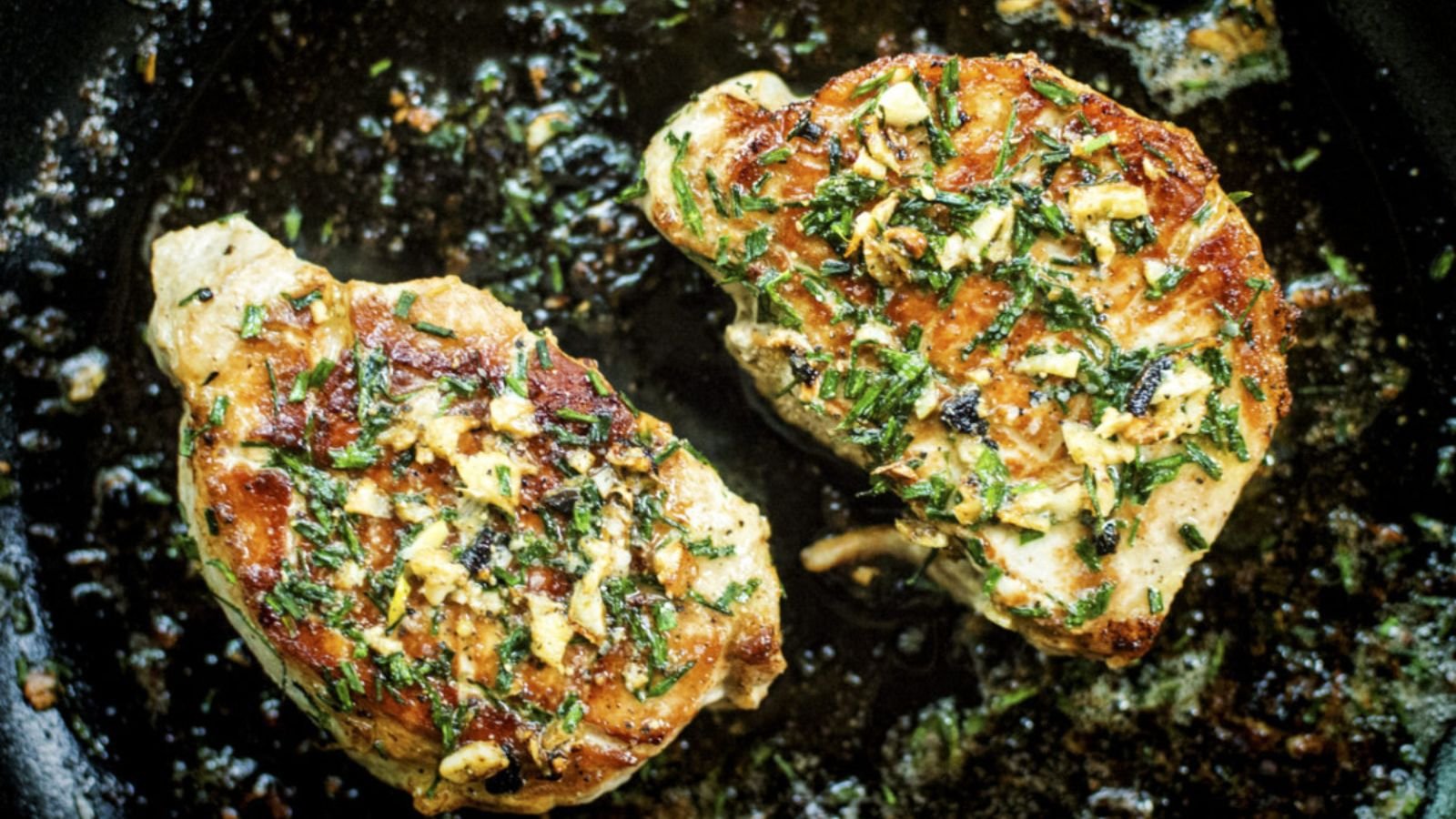 Pork chops pan-seared golden with butter and herbs coating the surface.