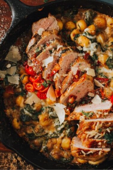 A cast iron skillet with sliced cooked meat, gnocchi, spinach, red peppers, and shaved cheese, placed on a wooden cutting board.