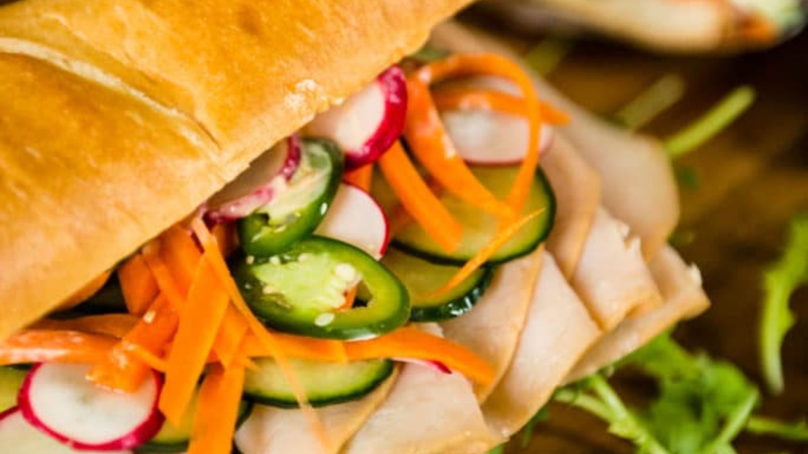 Banh mi sandwich filled with meats and quick pickled vegetables stacked neatly.