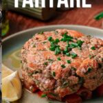 A plate of salmon tartare garnished with chopped chives and served with lemon wedges. Text reads: "How to make salmon tartare. Get the full recipe on girlcarnivore.com.