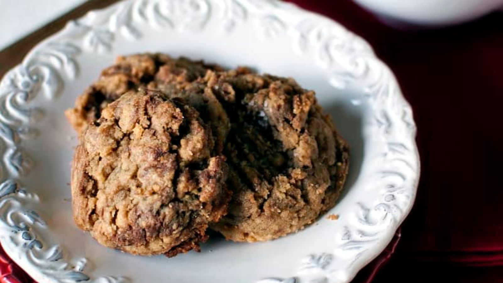 Two chocolate chip cookies on an ornate white plate.