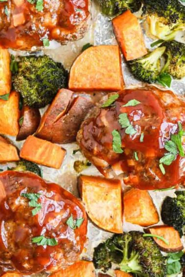 Sheet pan with three glazed meatloaves, roasted sweet potato cubes, and broccoli pieces on foil.