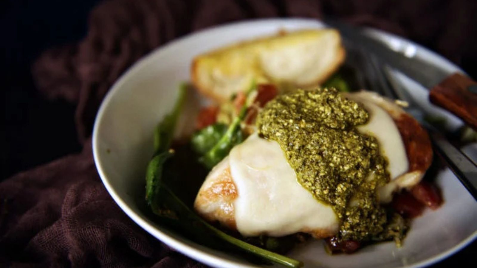Mozzarella chicken cooked in skillet with basil pesto melting.