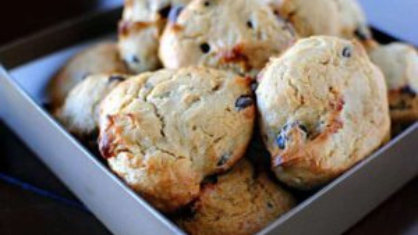 A box filled with several chocolate chip cookies resting on a dark surface.