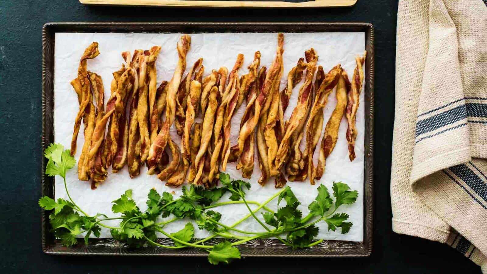 A tray lined with parchment paper holds strips of dried meat with sprigs of fresh cilantro placed at the bottom.