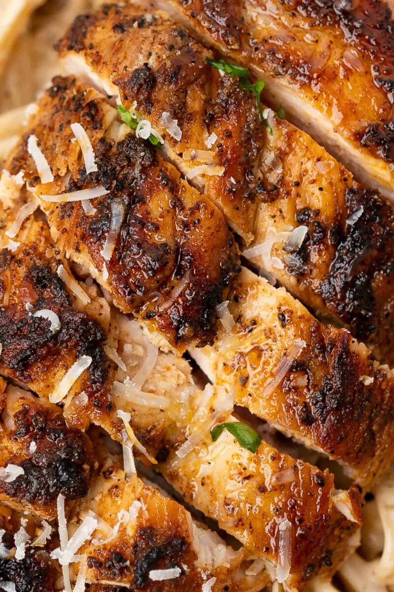 Close-up of sliced, seasoned blackened chicken breast topped with grated cheese, served over a creamy pasta.