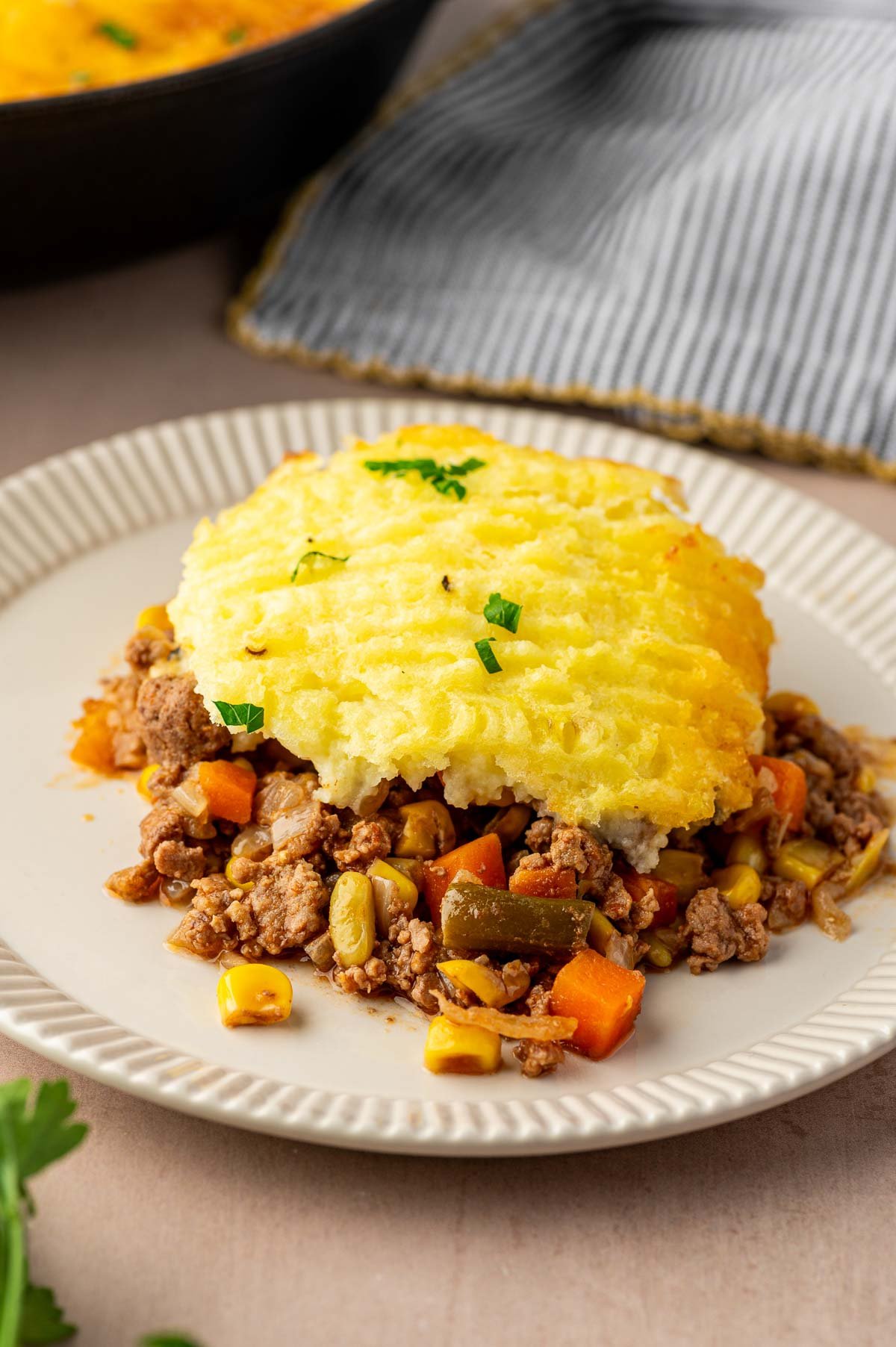 A serving of shepherd's pie with ground lamb, mixed vegetables, and a layer of mashed potatoes on a white plate.