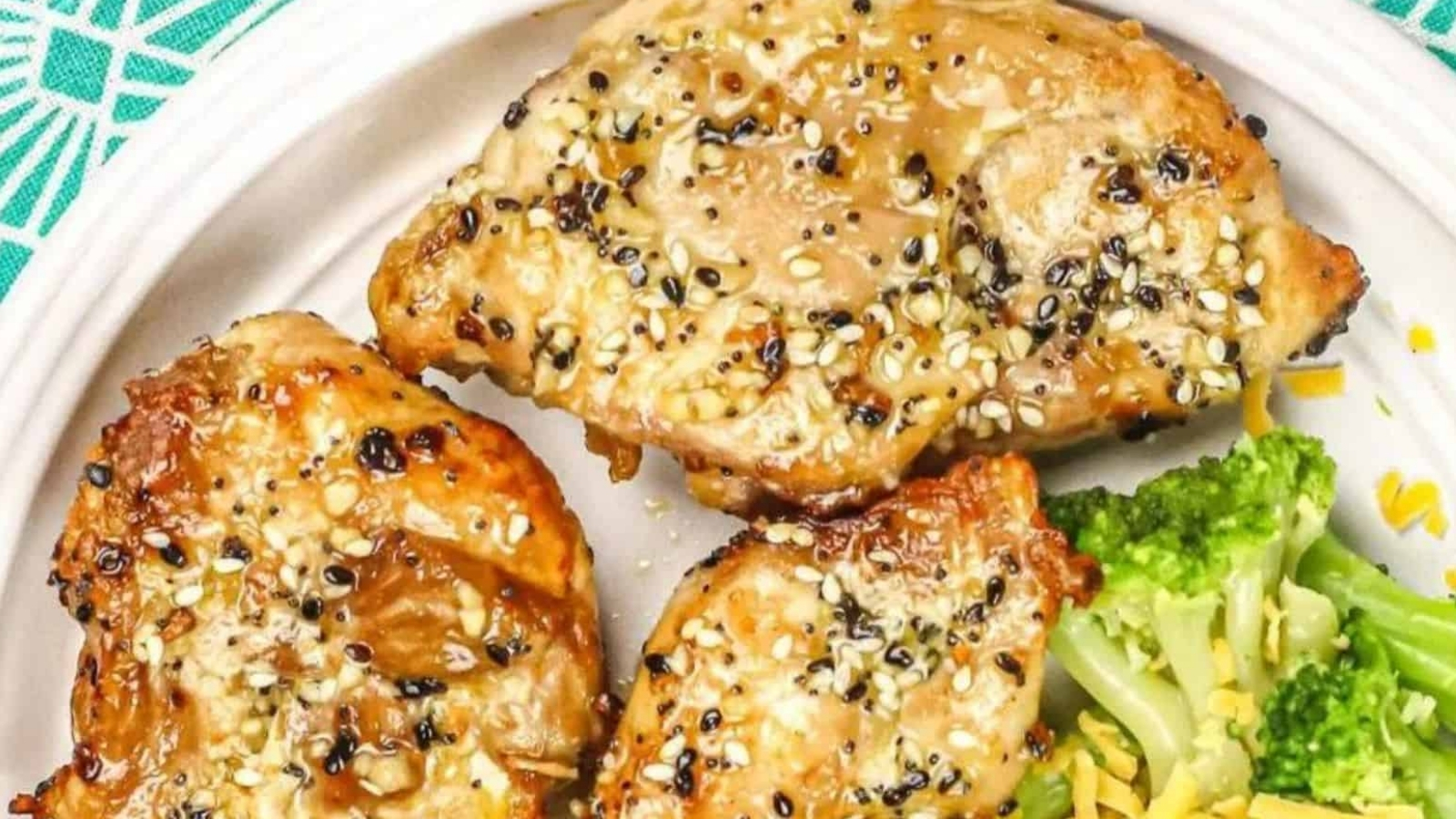 Three air-fried, sesame-crusted chicken thighs with broccoli on a white plate.