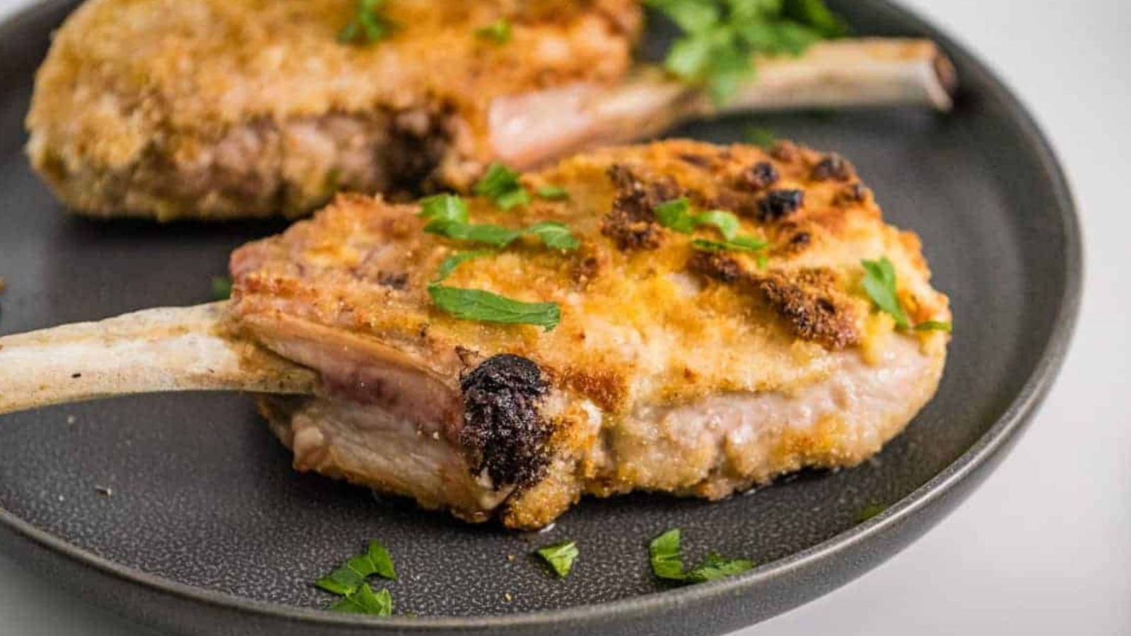 Two breaded pork chops on a gray plate with parsley.