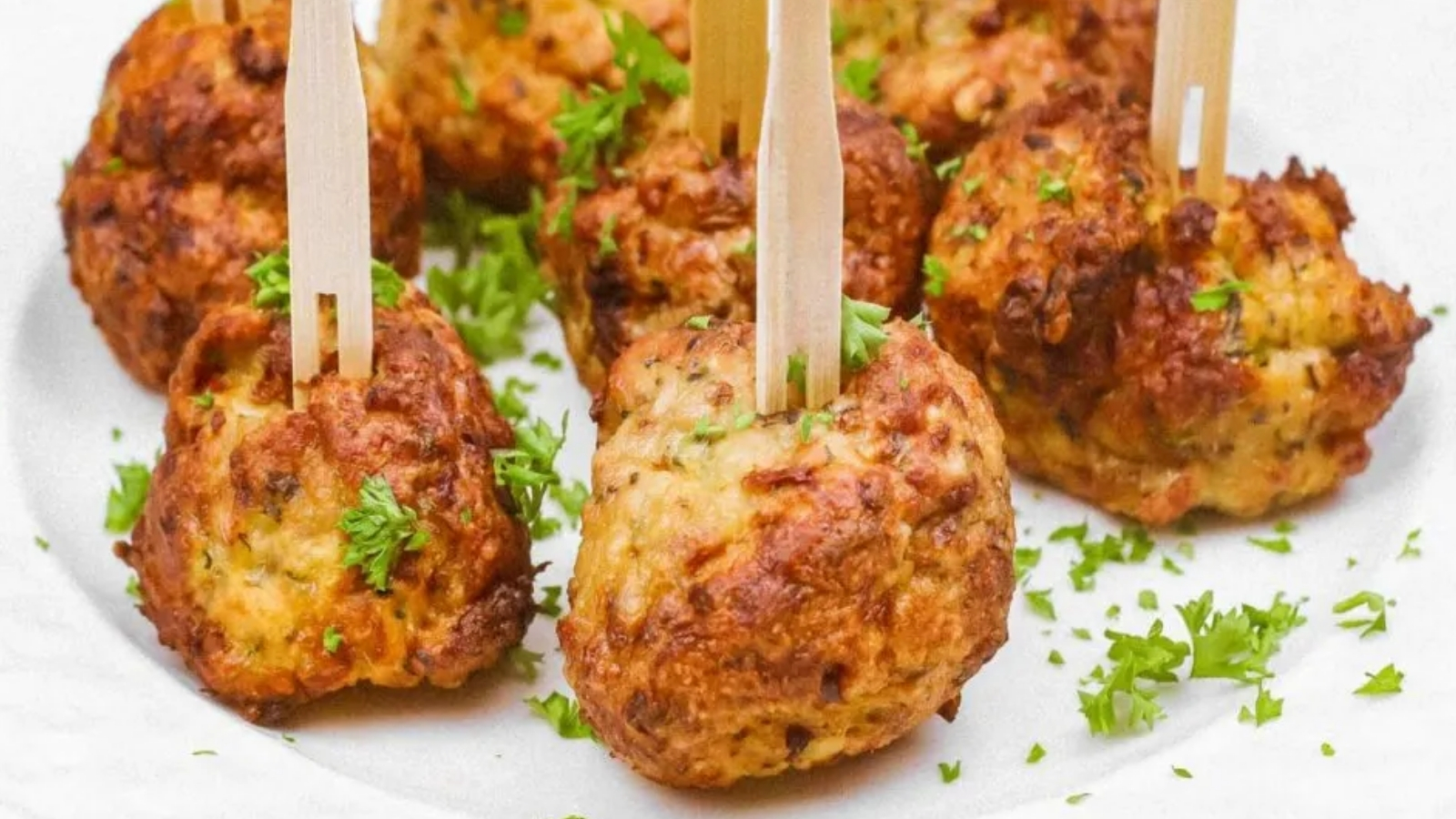 A white plate with several air-fried chicken meatballs garnished with parsley and wooden picks.