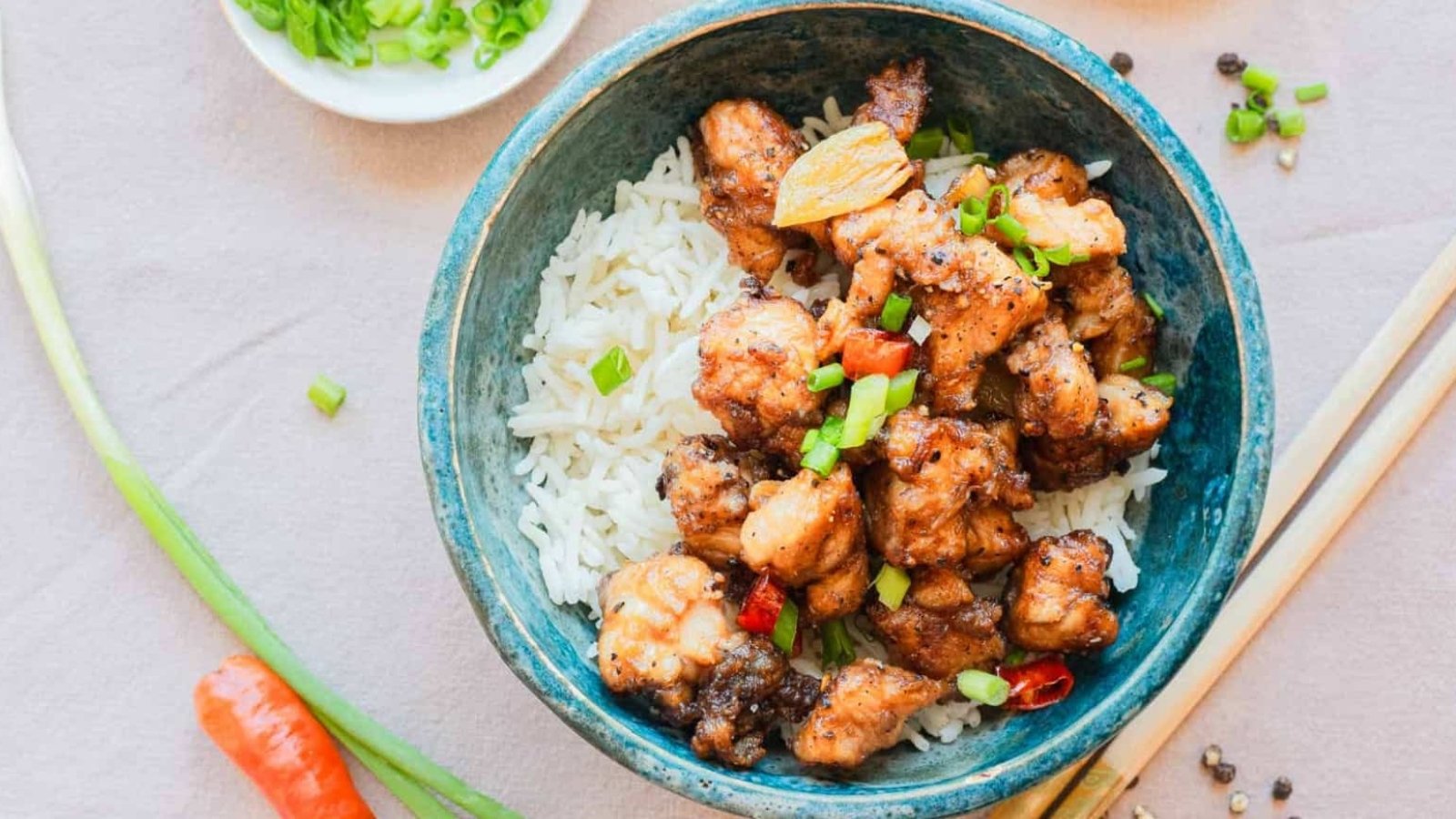 A bowl of white rice topped with stir-fried chicken pieces and chopped green onions, with chopsticks beside it.
