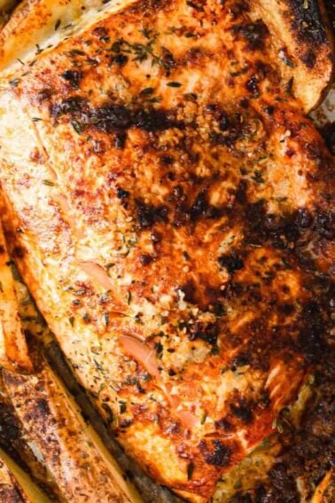 Baked salmon fillet surrounded by seasoned potato wedges on a parchment-lined baking sheet.