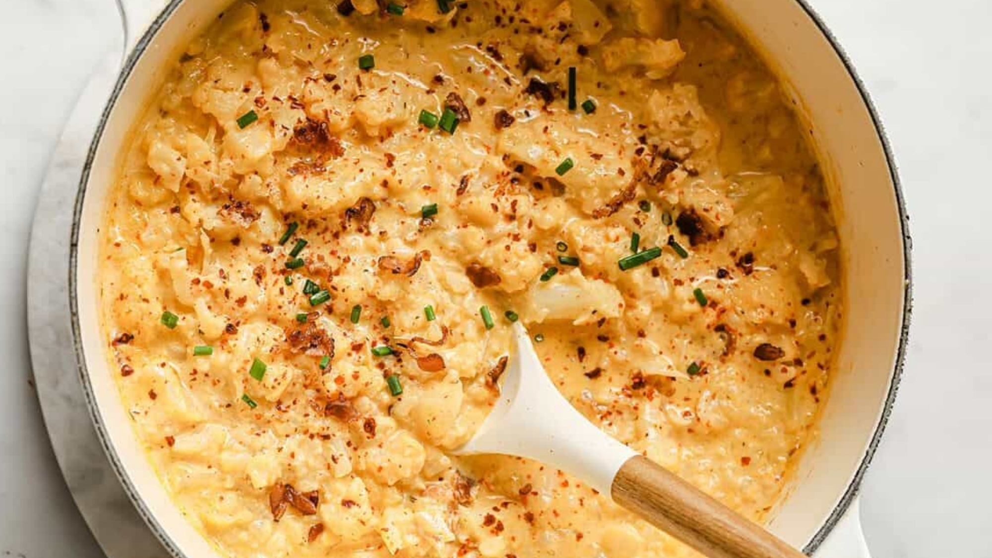 Cauliflower cheddar cheese bacon soup in a pot with a spoon.