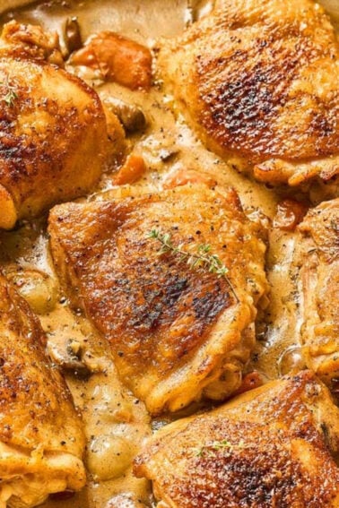Six browned chicken thighs simmer in a creamy sauce with mushrooms and vegetables in a large skillet.