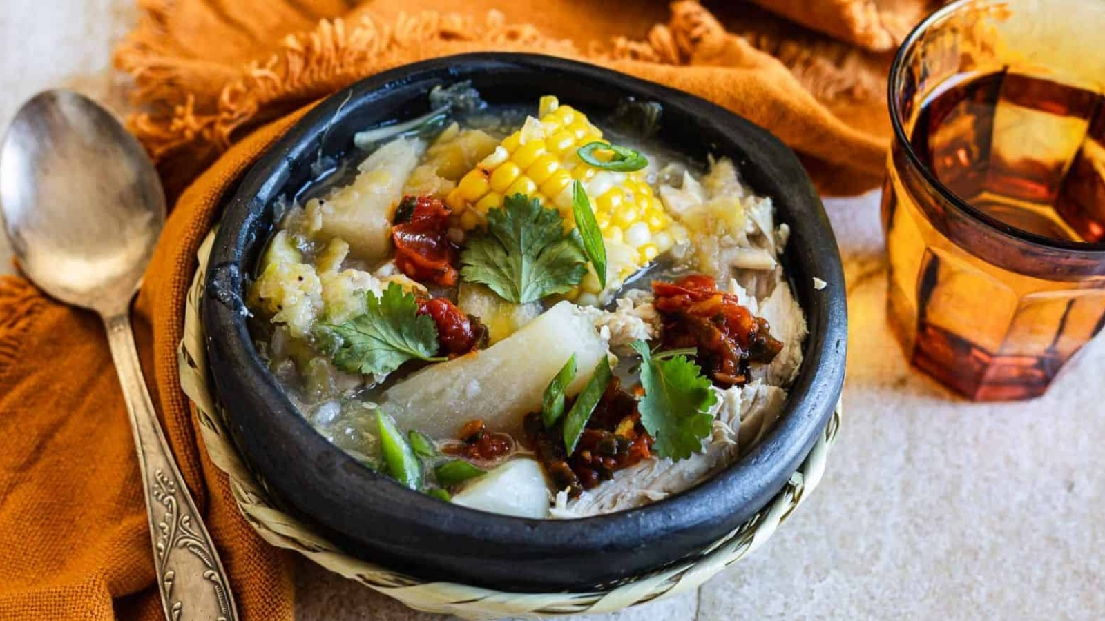 Bowl of chicken sancocho with corn, plantains, potatoes, and carrots in broth.