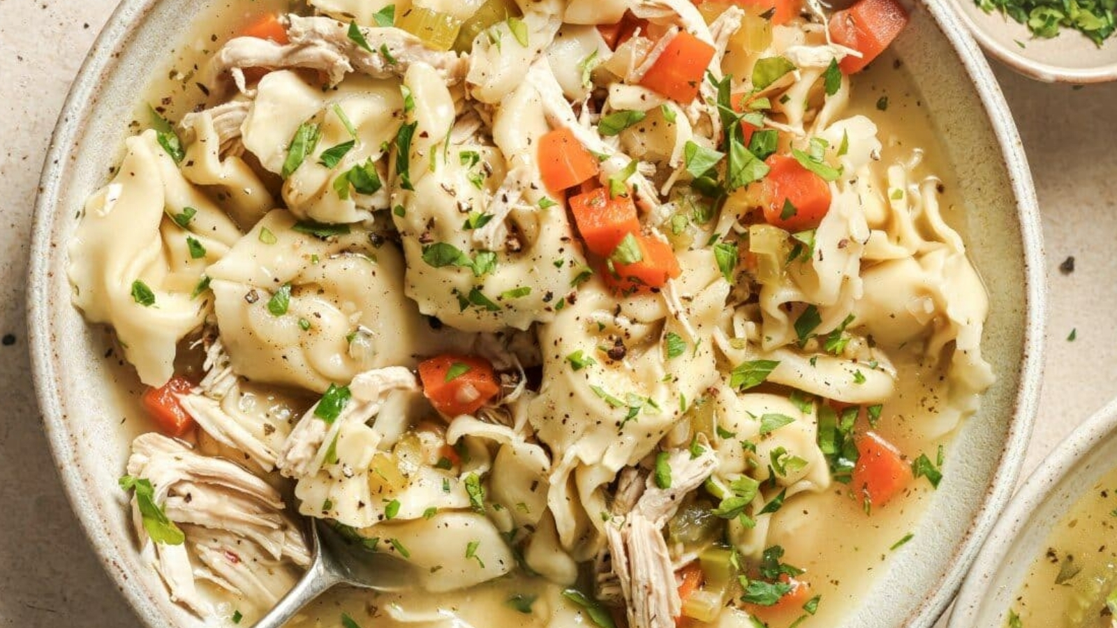 A bowl of chicken tortellini soup with vegetables and herbs.