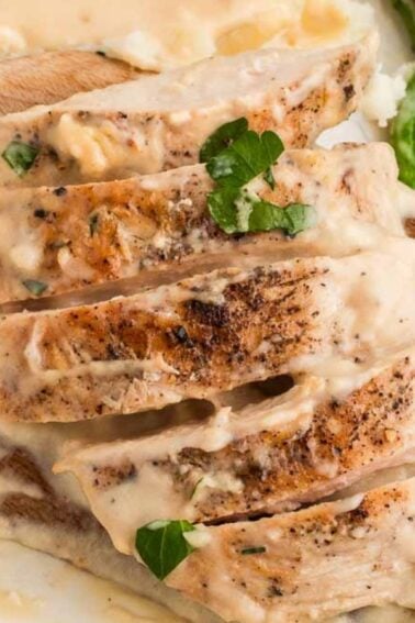 Sliced chicken breast with creamy sauce served over mashed potatoes, garnished with parsley, and a side of roasted asparagus—a comforting favorite among classic Meat Dinners.