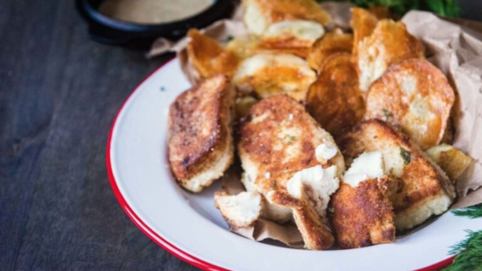 Fish fillets crusted with dill and potato fried to crisp golden texture beside thick-cut chips.