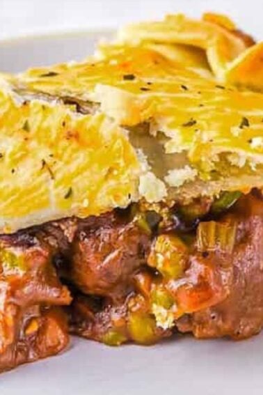 A slice of meat pie with flaky golden pastry, showing a filling of beef, vegetables, and gravy, served on a white plate.