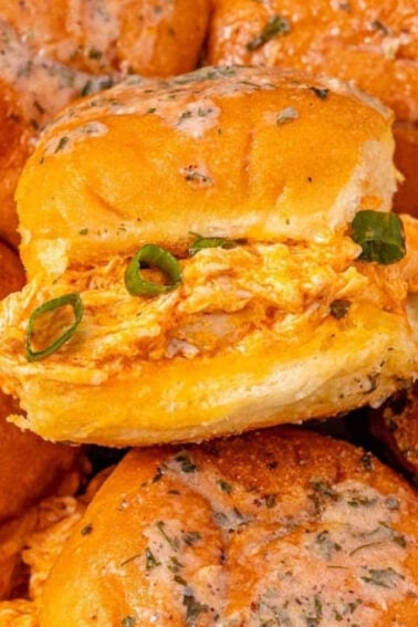 A plate of golden baked sliders filled with shredded chicken and topped with chopped green onions and a glaze.