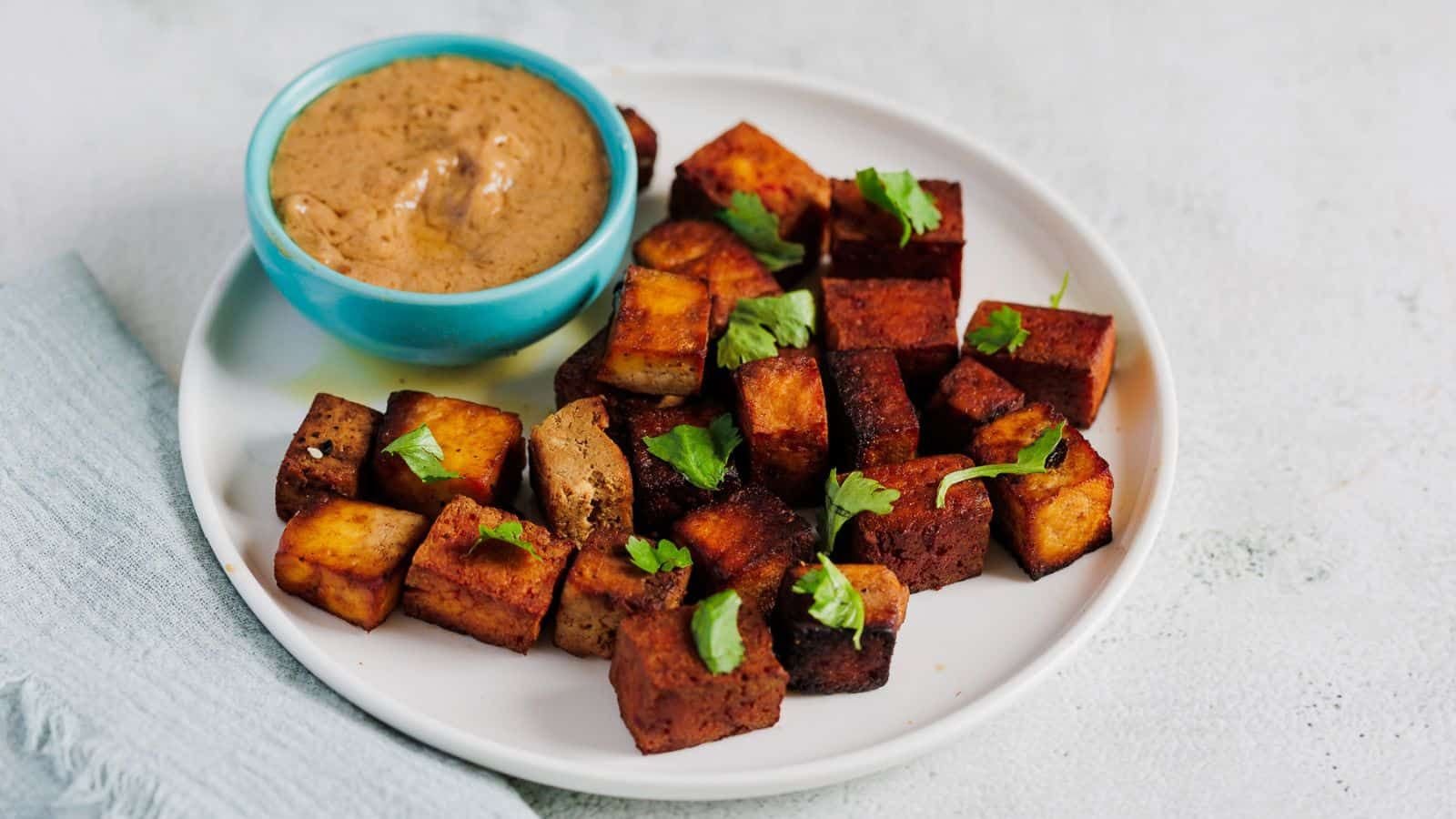 A fried marinated tofu on white plate with dipping sauce.