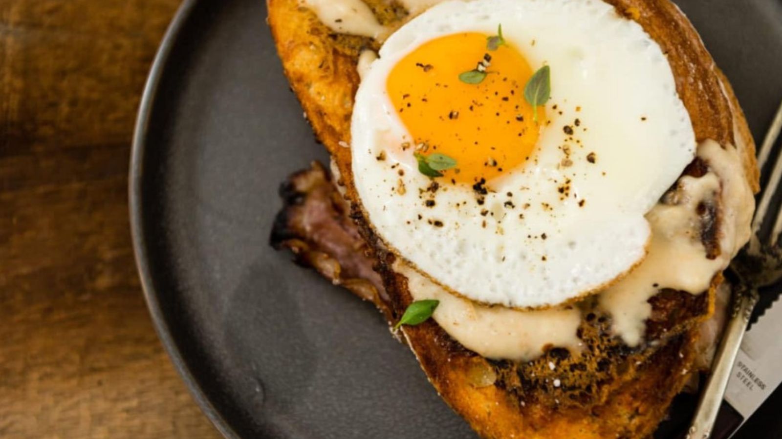 Croque Madame topped with melted cheese and fried egg dripping slightly.