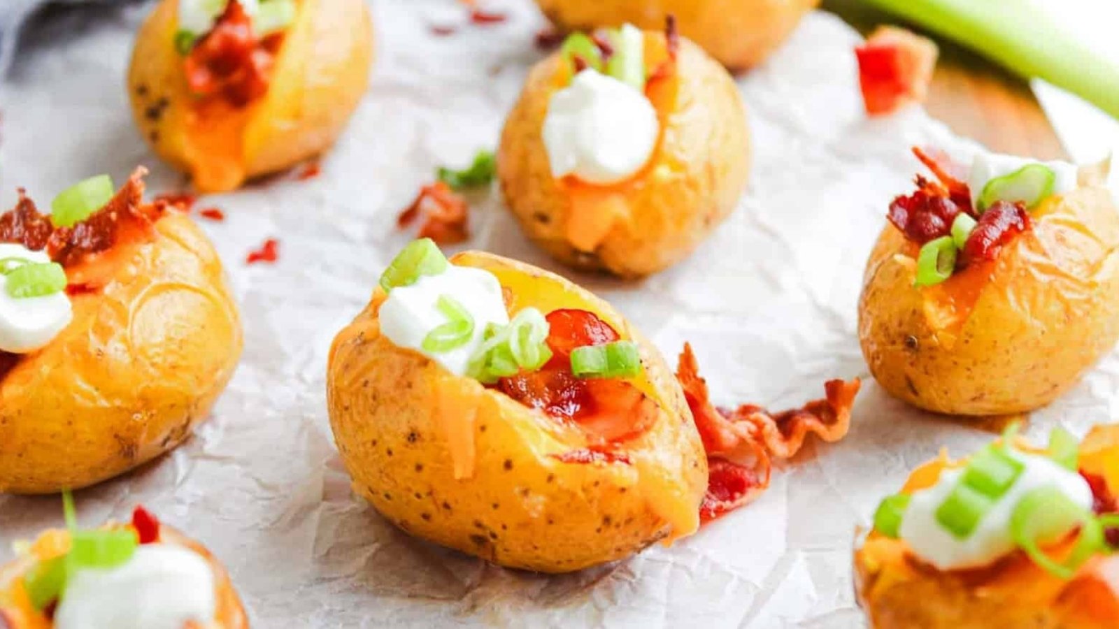 Mini baked potatoes topped with sour cream, bacon bits, cheddar cheese, and chopped green onions.