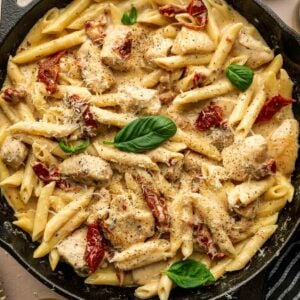 A skillet filled with marry me chicken pasta, loaded with chicken pieces, sun-dried tomatoes, creamy sauce, grated cheese, and garnished with fresh basil leaves.