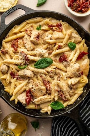 A skillet filled with marry me chicken pasta, loaded with chicken pieces, sun-dried tomatoes, creamy sauce, grated cheese, and garnished with fresh basil leaves.