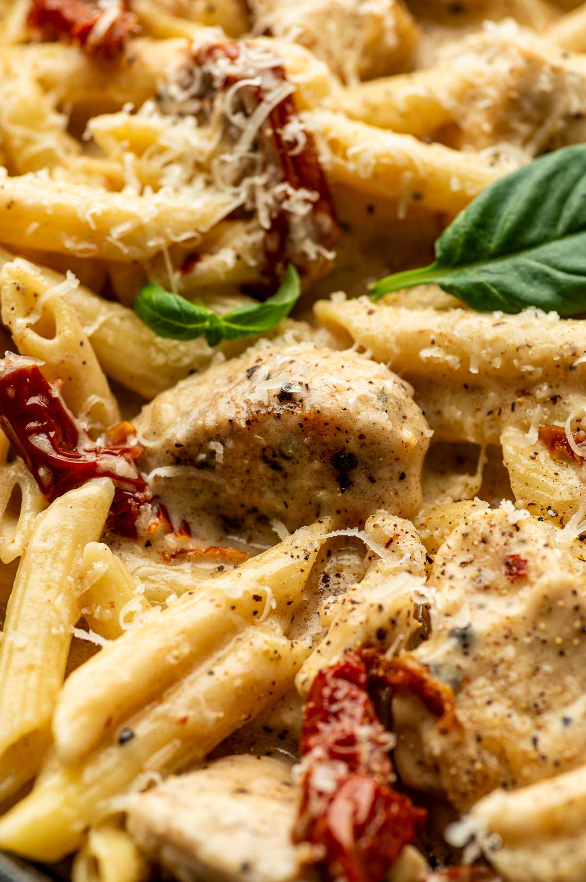 Close-up of creamy marry me pasta with pieces of chicken, sun-dried tomatoes, grated cheese, black pepper, and fresh basil leaves.