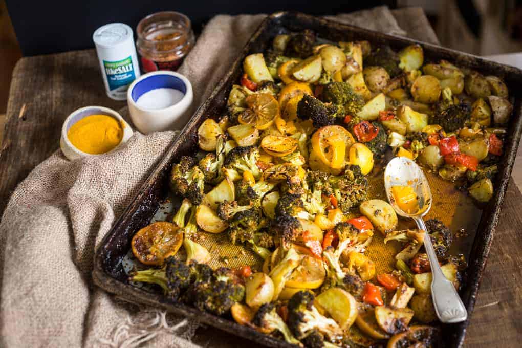 Roasted vegetables and lemon slices on a baking sheet, with a spoon and small bowls on the side.