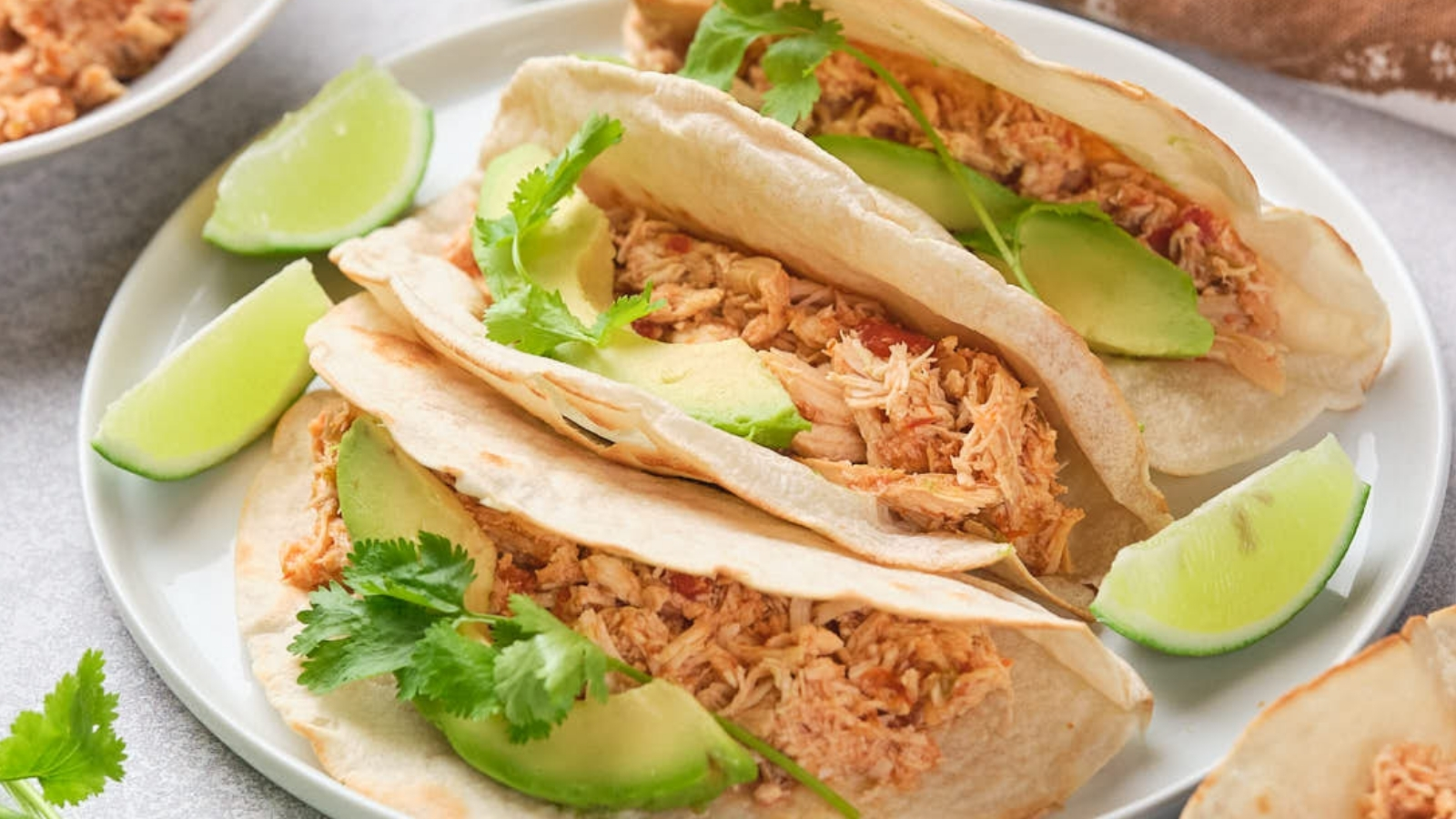 Close-up of shredded chicken with vegetables in a pan, being stirred with a wooden spoon.