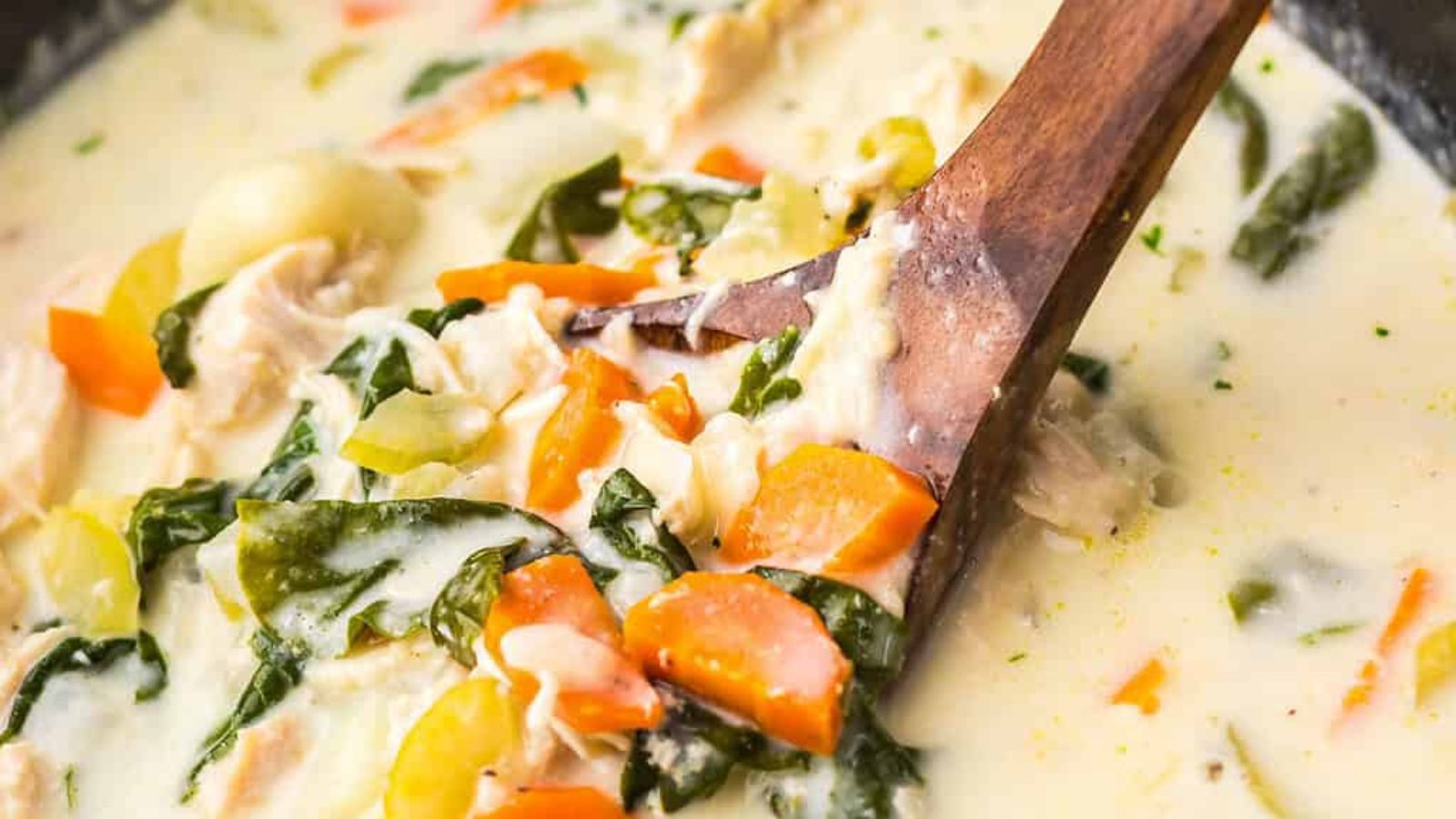 Creamy chicken gnocchi soup with vegetables served in a white bowl, bread and herbs on the side.