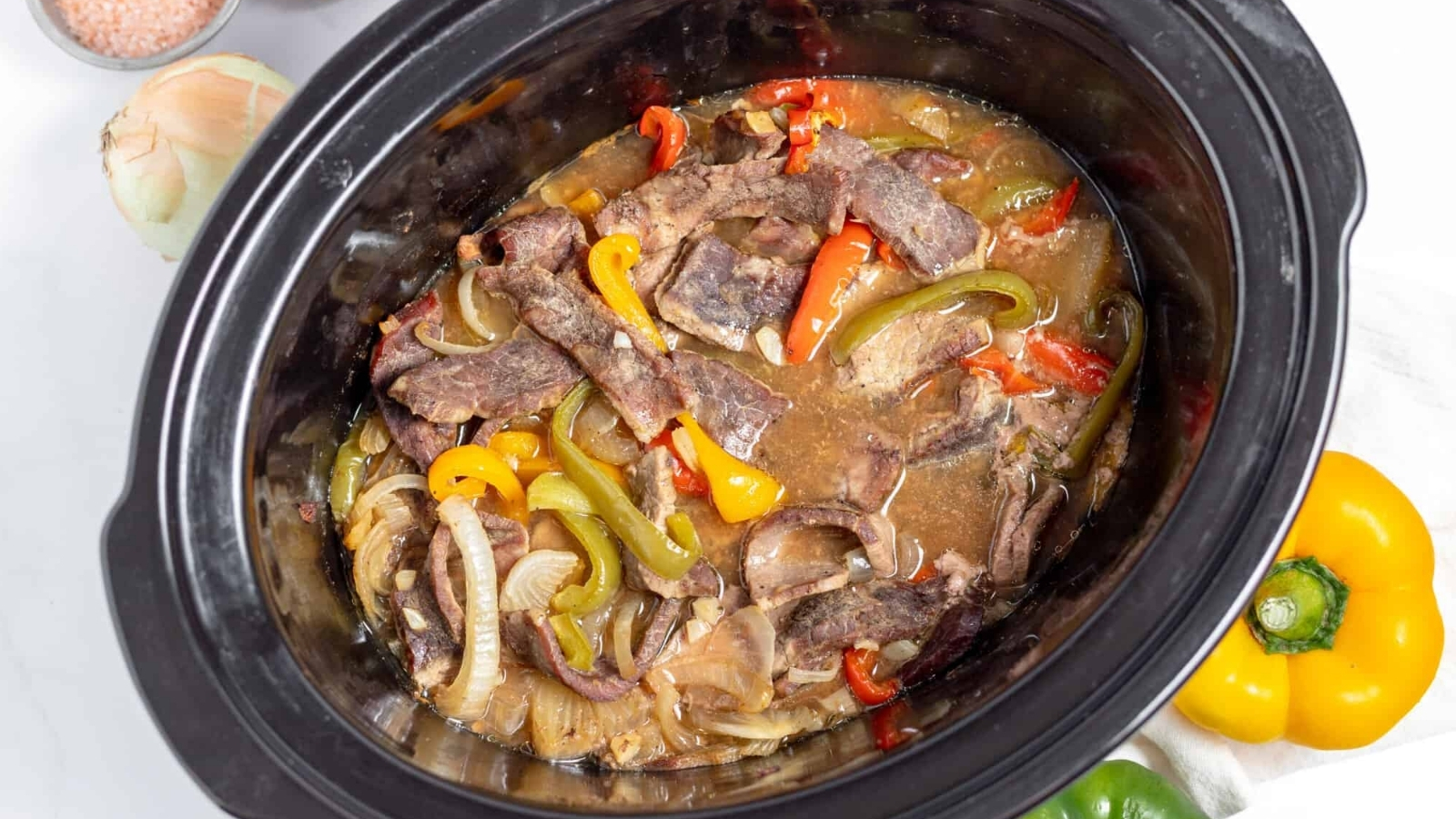 A crock pot filled with beef and peppers.
