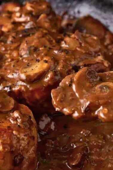 Chicken in a skillet topped with a creamy brown mushroom sauce, with a spoon lifting some of the sauce and mushrooms.