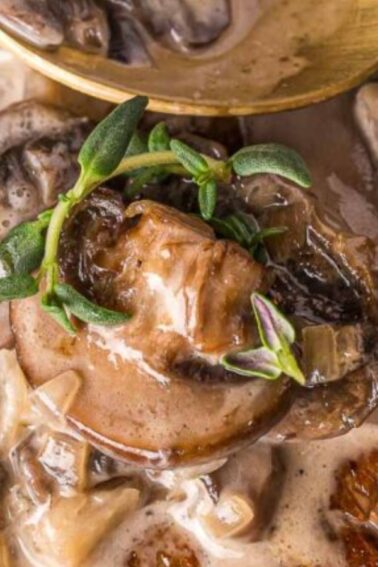 A close-up of a steak topped with creamy mushroom sauce and garnished with fresh herbs, as a spoon adds more sauce—a delicious example of Classic Dinners.