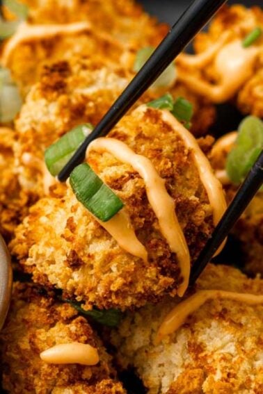 A plate of breaded, baked cauliflower bites drizzled with orange sauce, garnished with green onions, and served with a side of creamy dipping sauce—perfect for easy appetizers at any gathering.