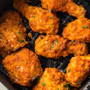 Seven pieces of crispy fried chicken with seasoning are arranged in the basket of an air fryer.