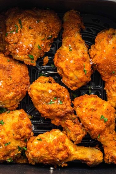 Eight pieces of golden-brown fried chicken with a crispy coating, garnished with parsley and salt, arranged in an air fryer basket.