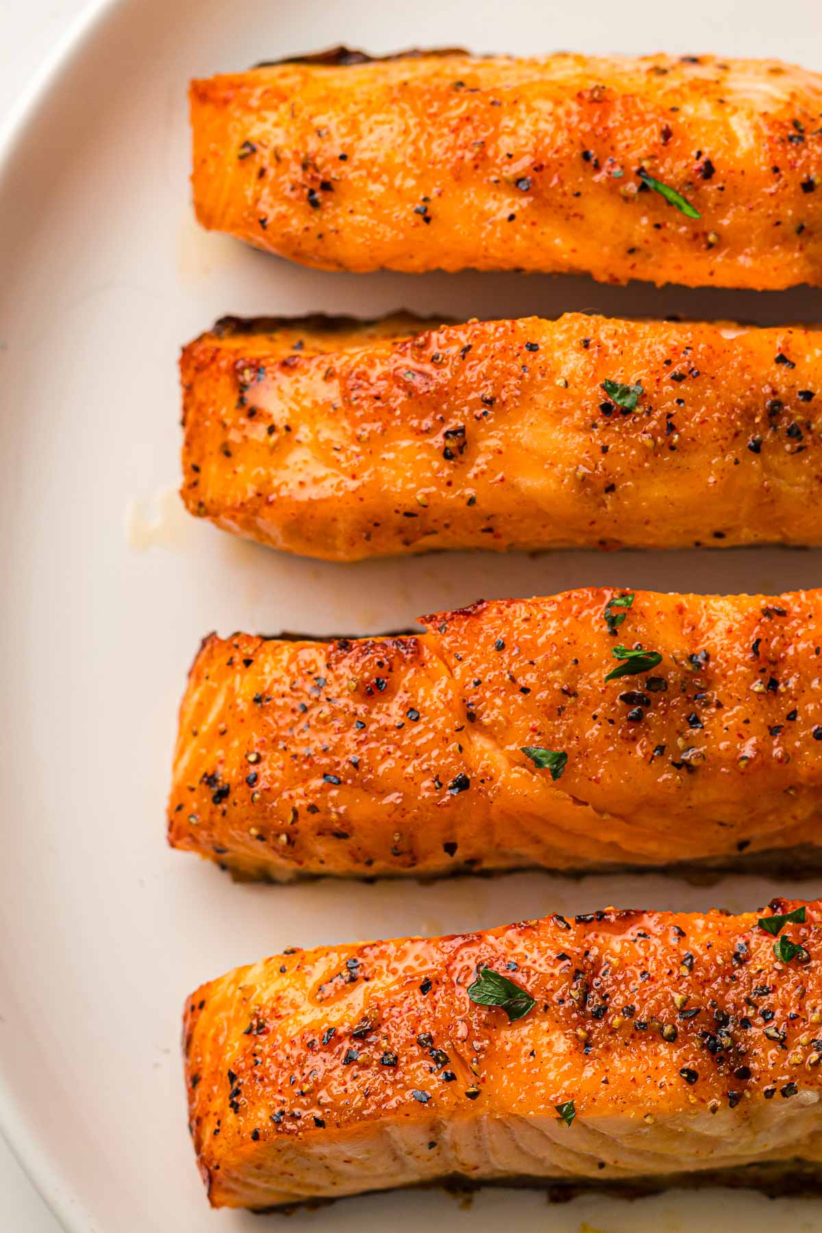 Three seasoned and air fried salmon fillets arranged in a row on a white plate.