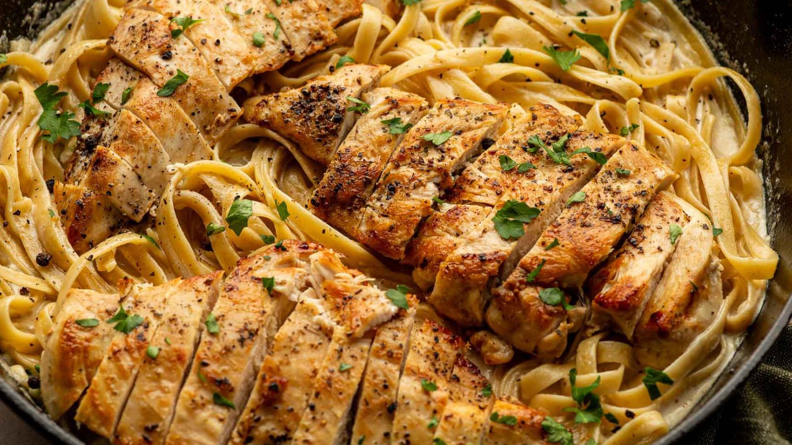 Pasta coated in creamy Alfredo sauce with sliced chicken.