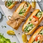 Overhead view of four shrimp rolls on a cutting board, garnished with herbs, next to celery, peppercorns, and dipping sauce. Text overlay reads: "How to Make East Coast Shrimp Rolls.